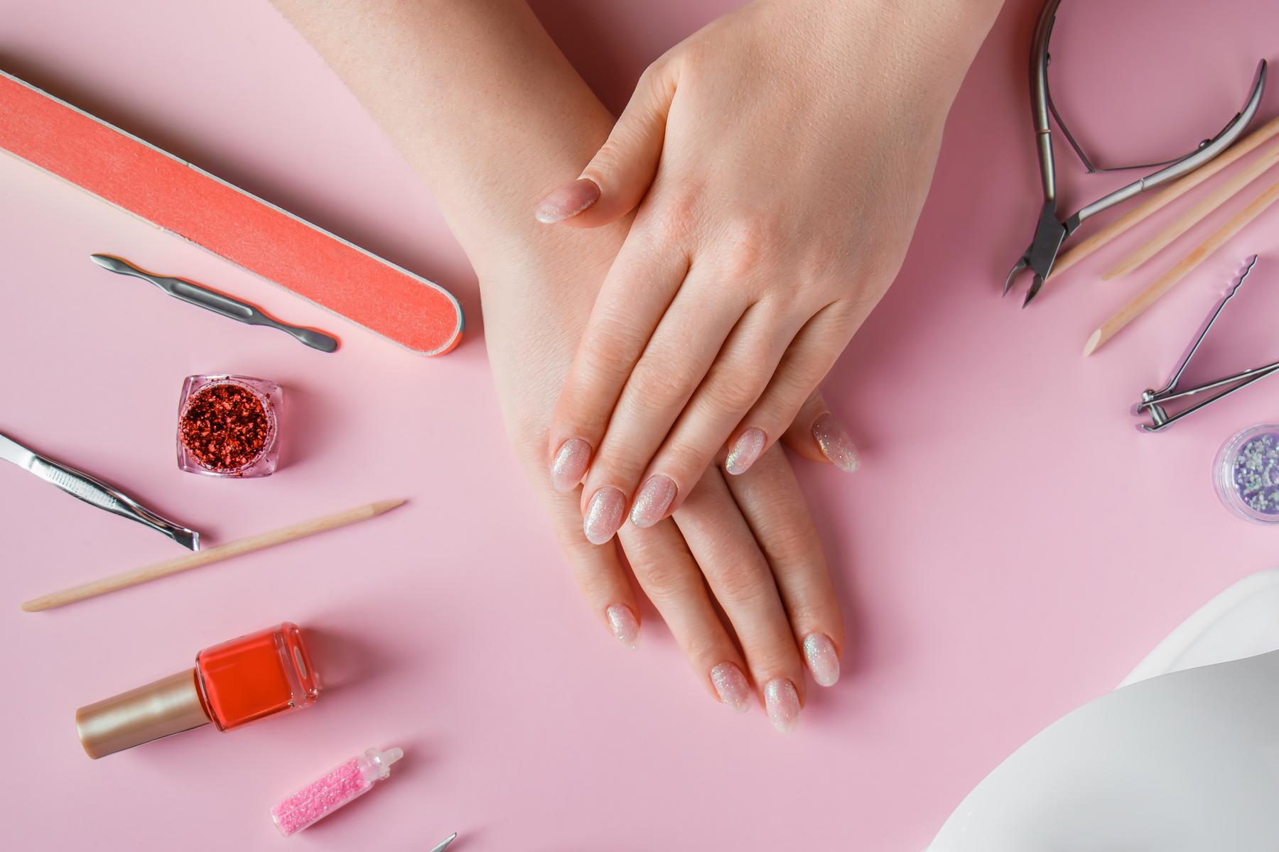 nail care procedure in a beauty salon. female hands and tools for manicure on pink background. concept spa bodycare.